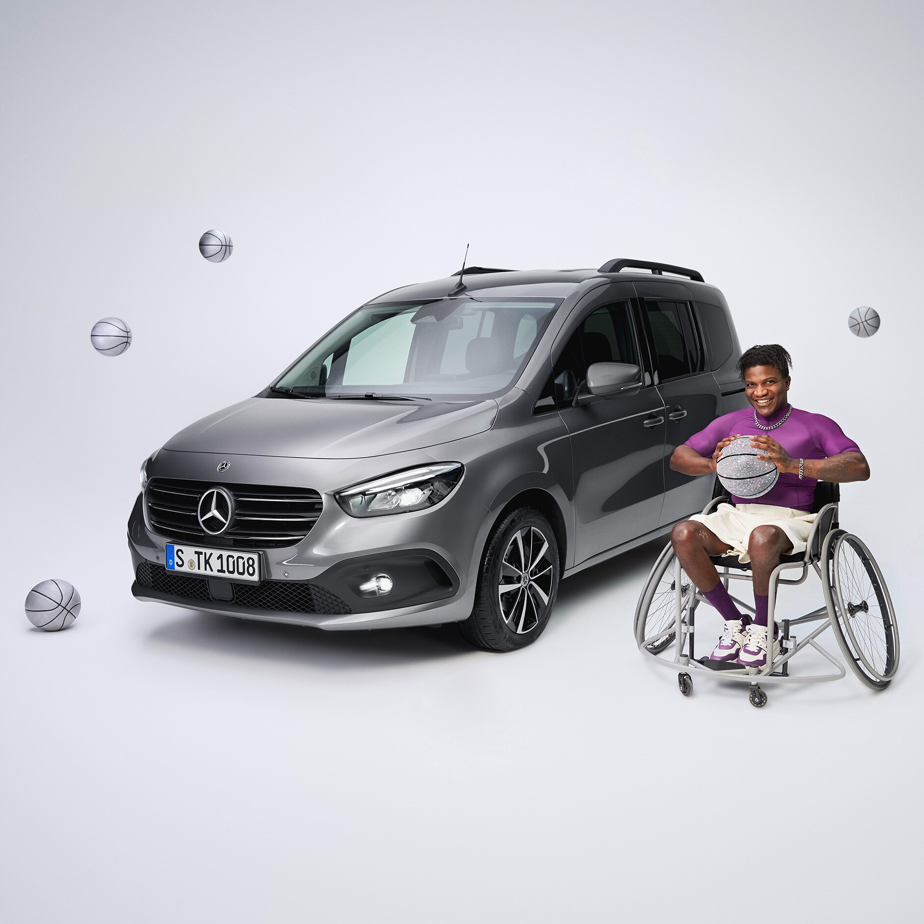 Poradenské služby | Jízdní pomocné prostředky | Mercedes-Benz Šikmý čelní pohled na Mercedes-Benz třídy T, který byl upraven pro tělesně postižené, a hráč košíkové na invalidním vozíku v popředí vlevo.