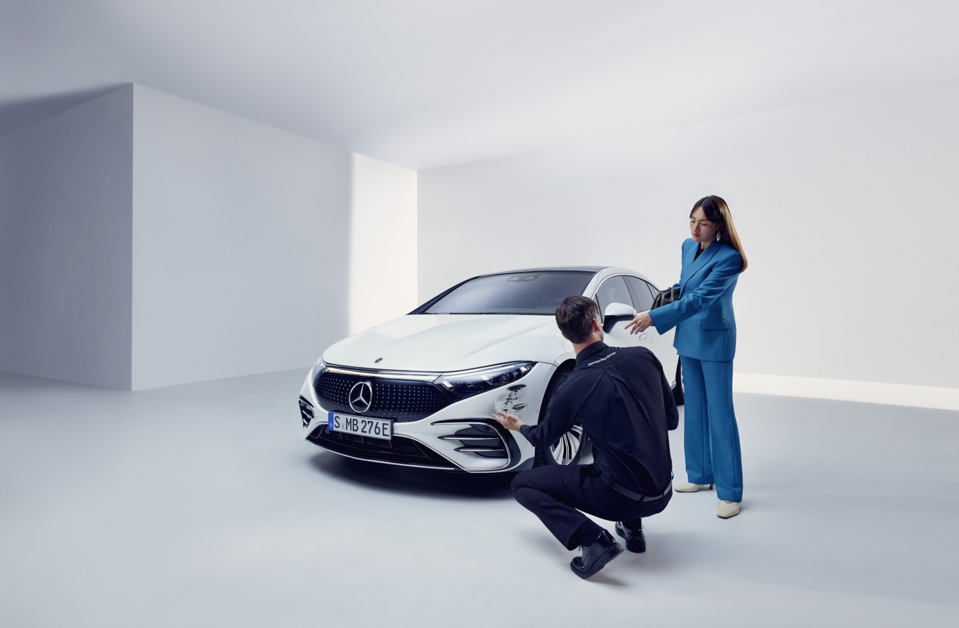 Oprava poškození | Mercedes-Benz Osoba z týmu podpory Mercedes-Benz klečí u poškozeného vozidla Mercedes-Benz.